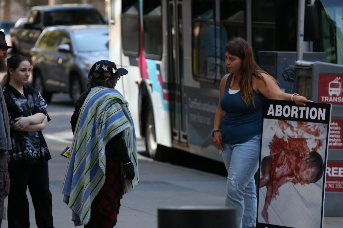 A pro-lifer holding a sign of an aborted child discussing the reality of abortion with the public in Vancouver.